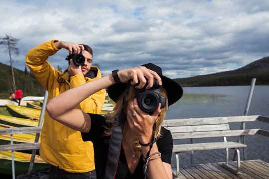 Finland, Lapland, man and woman taking pictures on jetty at a lake