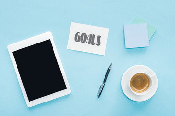 top view of digital tablet with blank screen, 'goals' lettering on card and sticky notes with blue background
