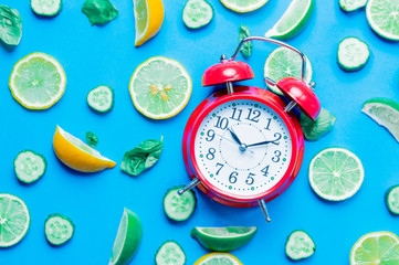 Above view at cutted lemons and limes and alarm clock on blue background