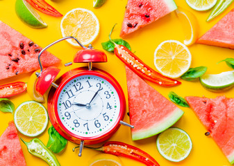 Above view at Watermelon and Chili pepper with lemons near alarm clock on yellow background