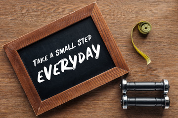measuring tape, dumbbells and wooden chalk board with 'take a small step everyday' quote, dieting...