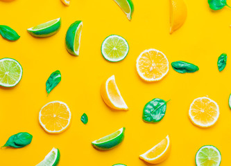 Above view at cutted lemons and limes with cucumbers on yellow background