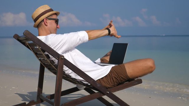 Young Man Working With Laptop Relaxing On The Beach On Vacation.