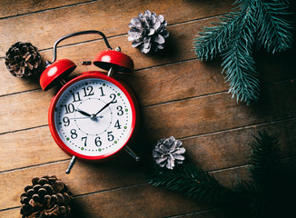Red Christmas alarm clock and pine cones with branches on wooden background