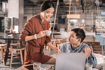 Woman holding cup of coffee working remotely with husband