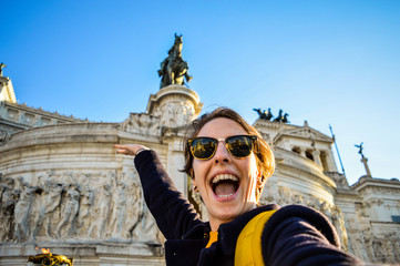Roma, Italy. Happy smiling young woman taking selfie with the front of a famous landmark in the background