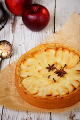 Traditional holiday apple pie. Baked dessert with anise, cloves and apples on light wooden background
