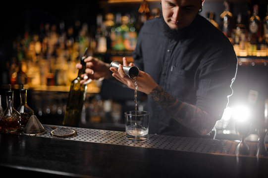 Bartender pouring a drink a cocktail from the steel jigger