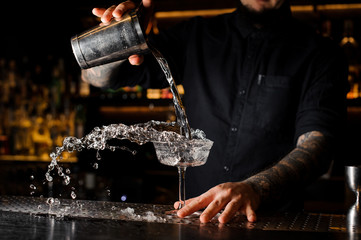 Bartender pouring a drink from the steel shaker to the glass