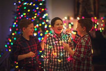 Brothers tying up each other in Christmas tree lights, low natural lighting