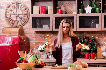 Girl with a displeased face is looking at broccoli in a bright loft kitchen. The girl does not like broccoli. Wooden plate with vegetables on a light wooden table.