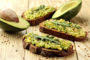 Avocado and arugula sandwiches closeup on natural wooden table. Sandwich with avocado puree.