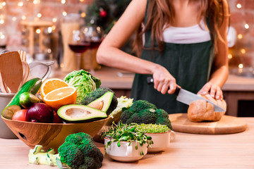 Girl in a green apron cuts the bread in a beautiful bright loft kitchen decorated with a garland....