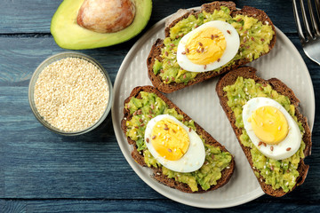 Sandwich with avocado puree and egg on a plate and ingredients for cooking on a blue wooden table. view from above