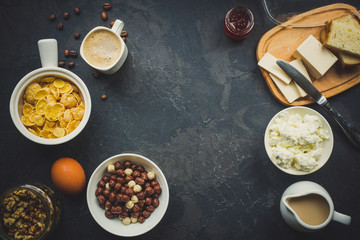 cornflakes, coffee, cottage cheese, bread, butter, eggs, jam and other ingredients for breakfast on a dark background. Top view with copy space