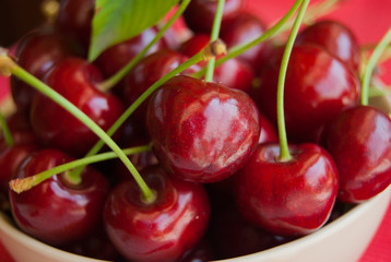 Foreground of bowl full of ripe and red cherries with petioles