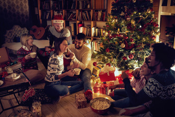 Group of friends sitting next to a Christmas tree, and having fun..