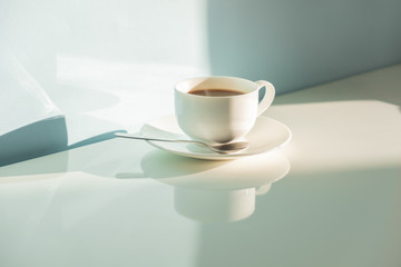 Cup of steaming coffee on seafoam green background in bright sunlight. Abstract photo of hot espresso drink on pale blue-green table and wall