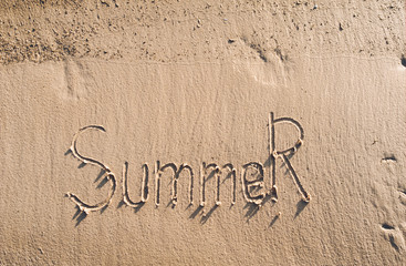 The word summer is written on the wet sand. The inscription is made by hand. Vacation concept.