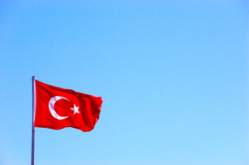 The national flag of Turkey flutters in the wind against a light blue sky