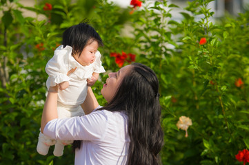 Fototapeta premium young happy and cute Asian Chinese woman enjoying and playing with her baby girl daughter holding her raising up in her arms smiling cheerful at garden resort