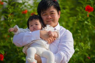 young happy and proud man as father of sweet little baby girl holding her daughter in front of flowers garden at holidays resort enjoying together outdoors