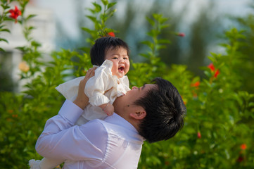 young happy and proud man as father of sweet little baby girl holding her daughter in front of flowers garden at holidays resort enjoying together outdoors