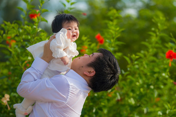Obraz premium young happy and proud man as father of sweet little baby girl holding her daughter in front of flowers garden at holidays resort enjoying together outdoors