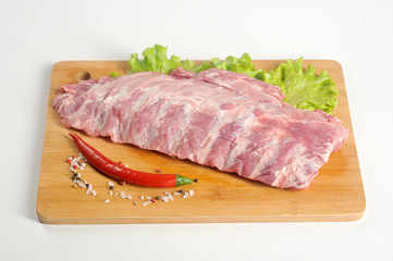 Pork ribs raw on a wooden board. The product is decorated with lettuce, spices, red pepper. White background. Close-up. 