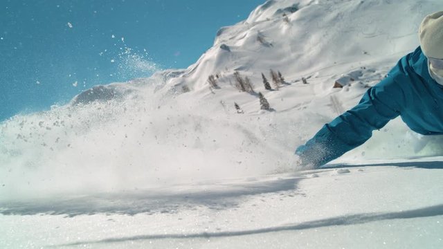SLOW MOTION SPEED UP, CLOSE UP: Smiling man snowboarding off piste drags his hand through the fresh powder snow. Stoked male on winter holiday having fun snowboarding cross country on a sunny day.