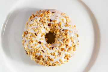 Donut with white chocolate and sprinkled with nuts on top, laid on white glossy plate.