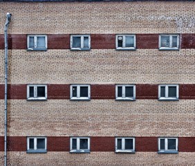 Naklejka premium Brick wall with brown stripes and lots of wooden windows in white frames. Urban world view