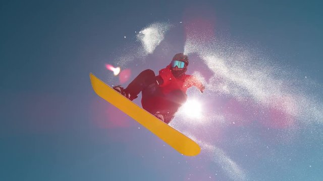 SLOW MOTION TIME REMAP, CLOSE UP, LENS FLARE: Bright winter sun shines on male snowboarder doing a pro spinning grab. Extreme man jumps off kicker and does a cool trick while riding in ski resort.