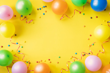 Heap of colorful balloons, confetti and candies on yellow table top view. Birthday party background. Festive greeting card.