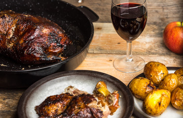 goose baked with apples and potatoes, next to a glass of red wine on a wooden background, rustic table