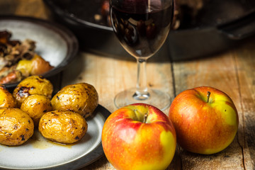 goose baked with apples and potatoes, next to a glass of red wine on a wooden background, rustic table