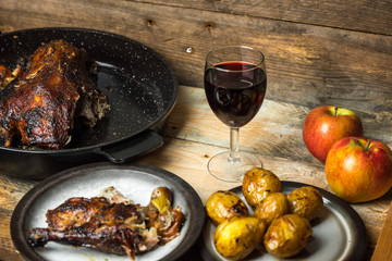 goose baked with apples and potatoes, next to a glass of red wine on a wooden background, rustic table