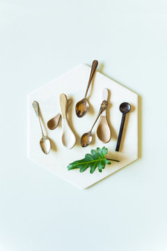 A still life flat-lay arrangement of various spoons on a white hexagonal tile, on a mint green  background.
