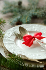 Antique or rustic table of Christmas tables from above. Elegant empty white plate, cutlery, red bow and natural pine on a wooden table.