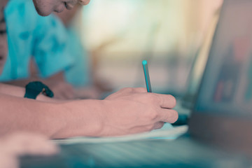 Male teacher in yellow shirt going around class, helping and che