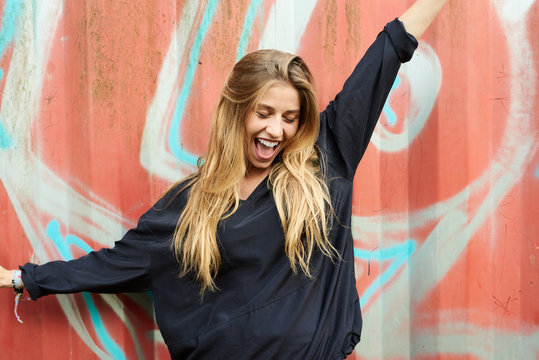 Cheerful blonde girl with outstretched arms smiling over graffit