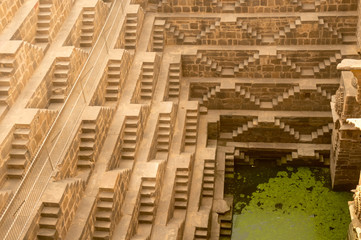 Steps leading down to the green water in abhaneri boari stepwell in jaipur rajasthan. The sandstone palace, arches, steps is a water source for the cities nearby