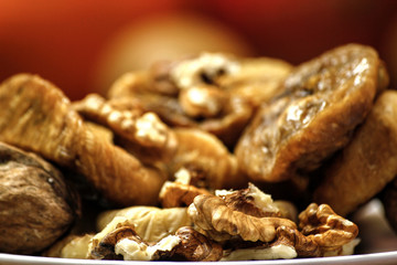 Dried fig and whole and cracked walnuts on white ceramic plate. Wooden table and various citrus in the background.