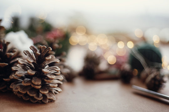 Pine cones on background of christmas wreath,lights, fir branches, red berries, thread, scissors, cotton,on rustic wooden background. Space for text. Atmospheric image