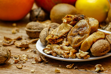 Dried fig and whole and cracked walnuts on white ceramic plate. Wooden table and various citrus in the background.