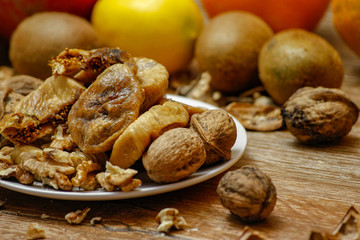 Dried fig and whole and cracked walnuts on white ceramic plate. Wooden table and various citrus in the background.
