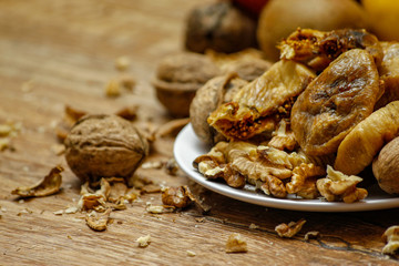 Dried fig and whole and cracked walnuts on white ceramic plate. Wooden table and various citrus in the background.