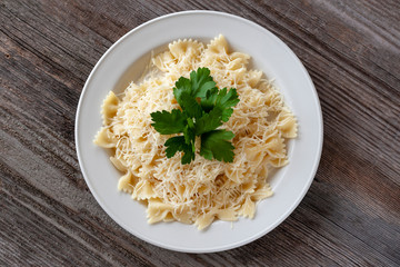 Healthy diet. Farfalle Pasta with cheese on a white plate, decorated with herbs. The view from the top. On a wooden table.