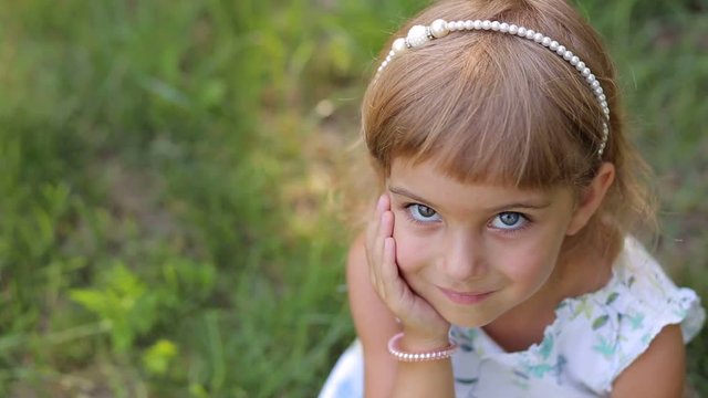 Portrait of cute smiling little girl in Park on green grass background. The view from the top. Heterochromia.