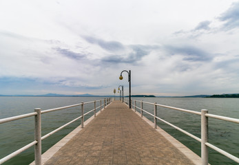 Fototapeta premium Beautiful view of Lake Trasimeno from the pier. The sky is clouded over and calm water, no people. Nostalgic mood. Umbria, Italy